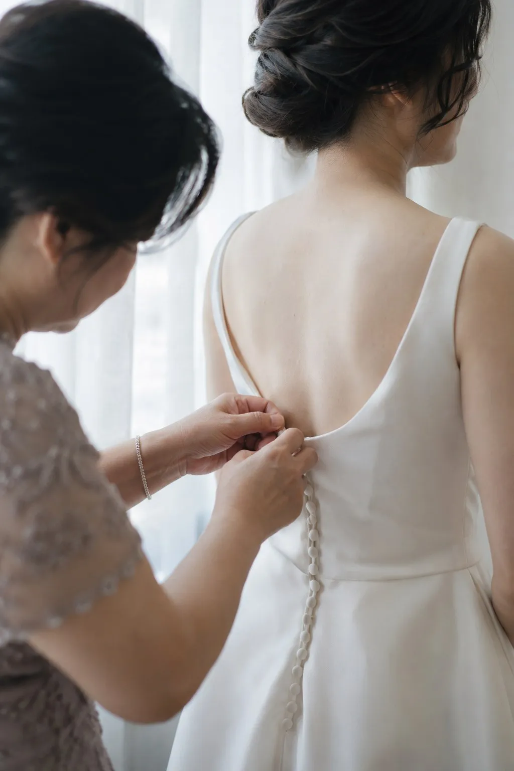 窗邊，媽媽幫穿白色禮服的新娘扣背後的扣子