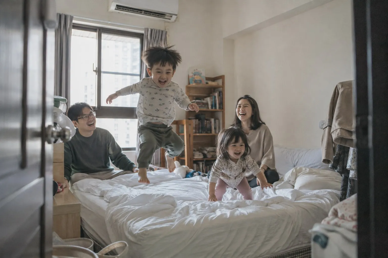臥室的床上，小男孩跳在半空，爸爸、媽媽和妹妹在笑